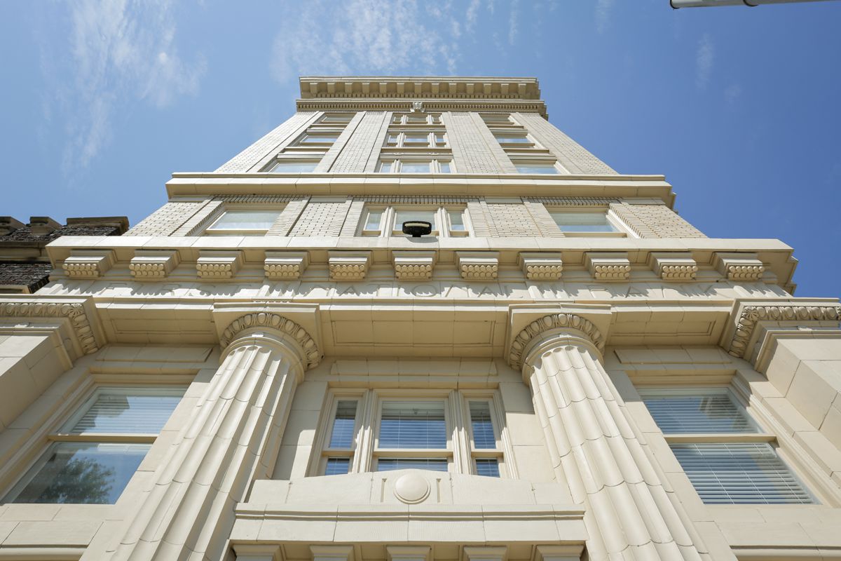 Low-angle view of a tall, light building with large columns and decorative moldings against a blue sky with scattered clouds.