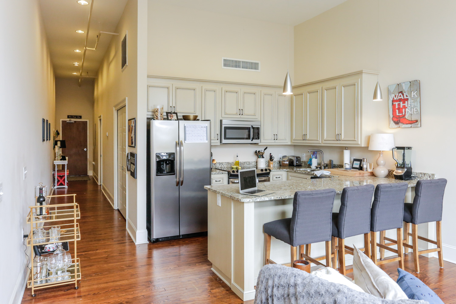 Modern kitchen with white cabinets, stainless steel appliances, granite counters, gray barstools at island, wood floors, and decor.