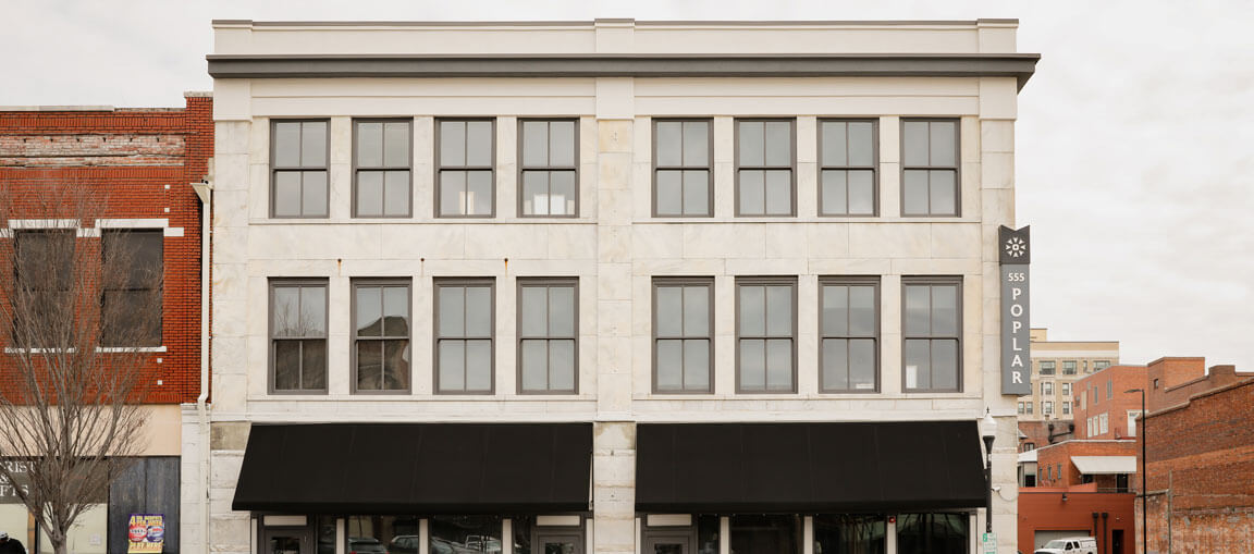 A three-story building with a white stone facade, large windows, black awnings, and a vertical sign reading 355 POPLAR; red-brick neighbors.