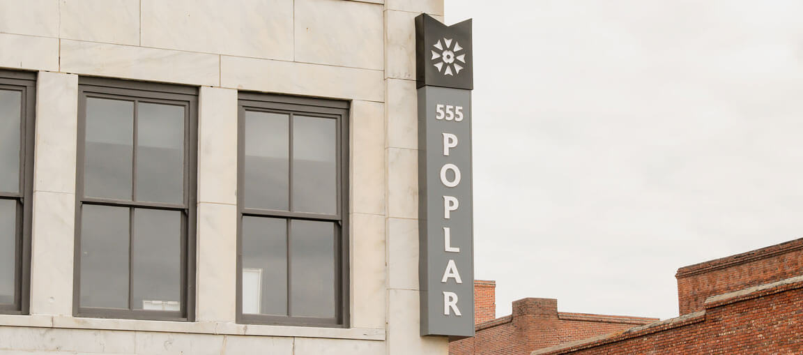 A vertical sign on a building reads 555 POPLAR with a decorative starburst at the top. The light stone building has large windows; brick buildings are in the background.