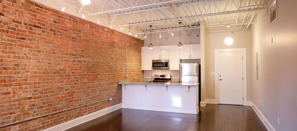 Modern loft with exposed brick, dark wood floors, open kitchen with white cabinets, stainless appliances, and industrial lighting.