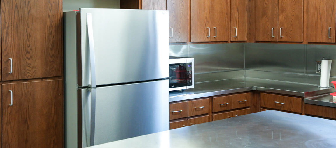 Modern kitchen featuring wooden cabinets, stainless steel refrigerator, microwave, metal countertops, and a paper towel holder.