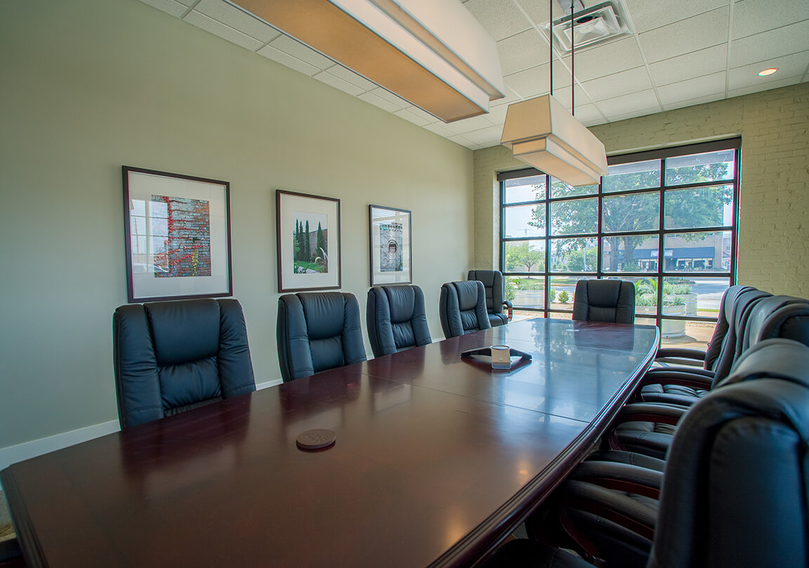 a conference room with 10 chairs at a long wooden table, and large garage door style window