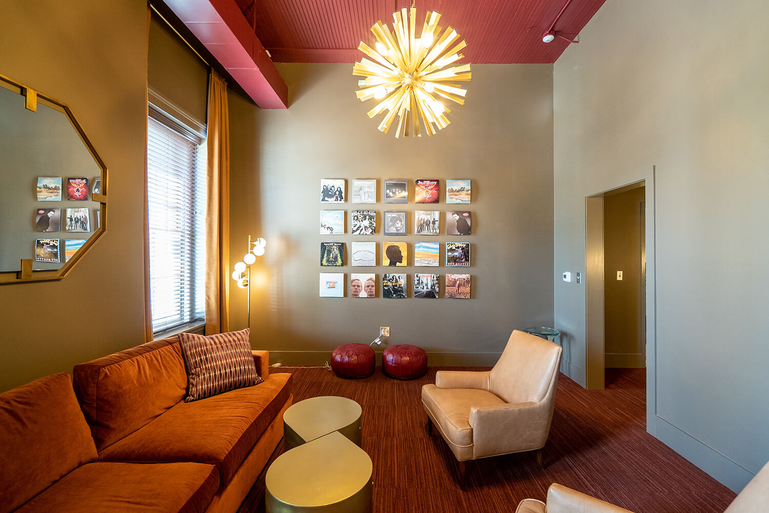 Modern living room featuring a red sofa, beige armchair, gold tables, starburst chandelier, photo wall art, and sunlit windows.