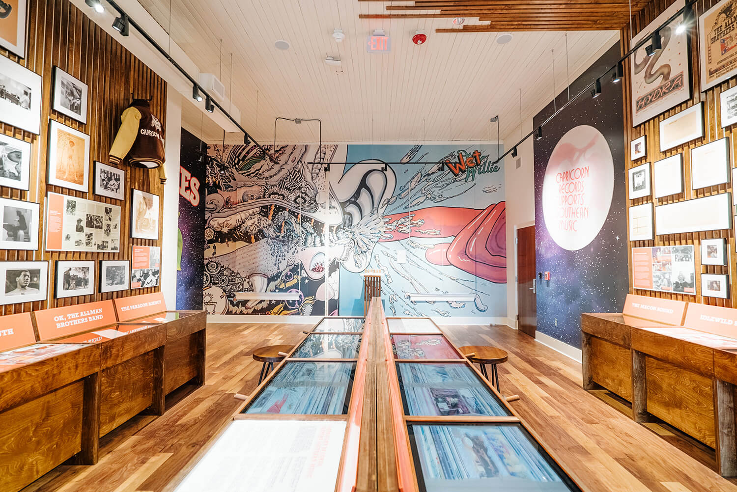 A brightly lit museum exhibit displays comic art, wooden benches, informative displays, and framed pictures, celebrating comics history.