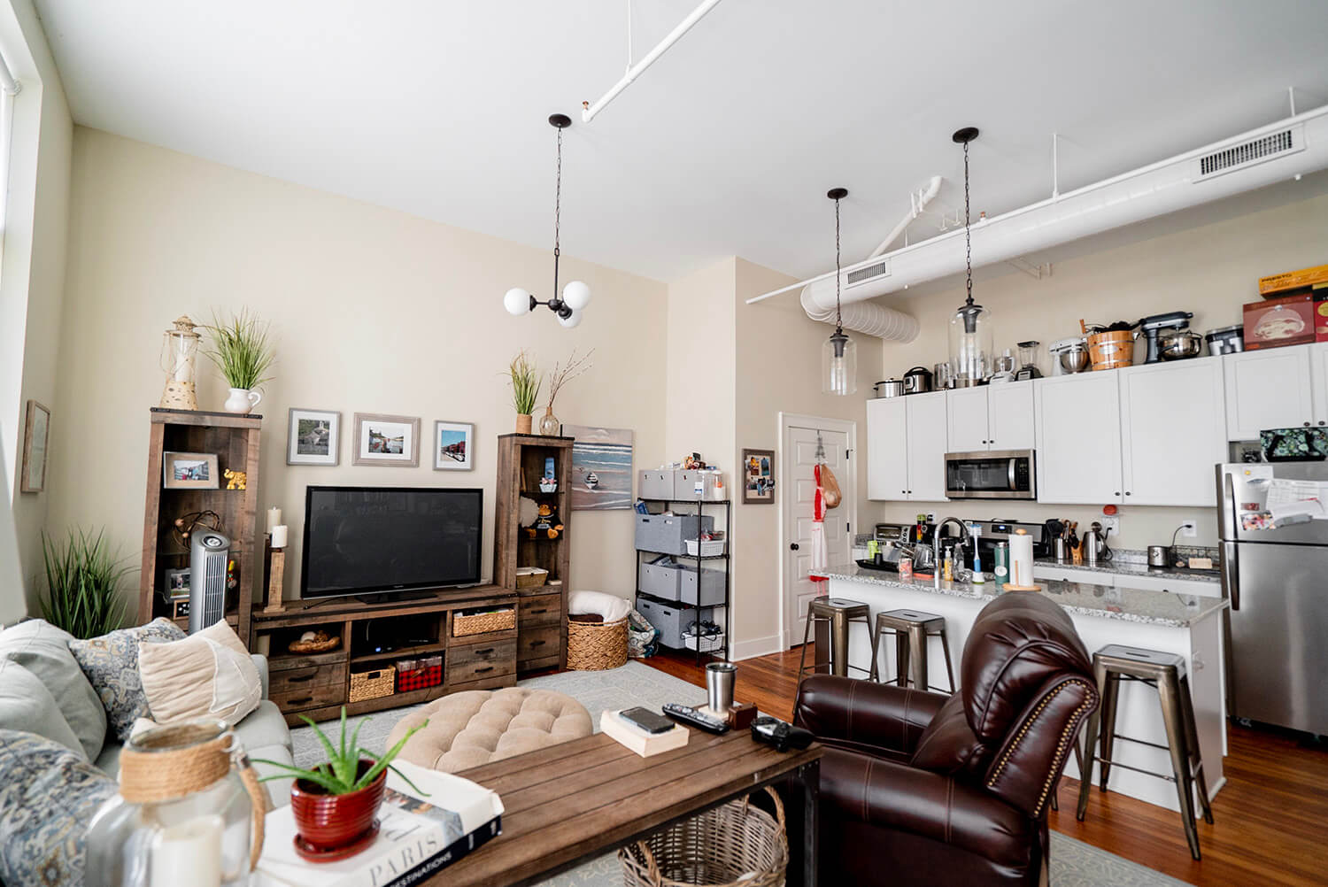 Cozy modern apartment with open floor plan, living area with TV, bookshelves, leather recliner next to kitchen and breakfast bar.