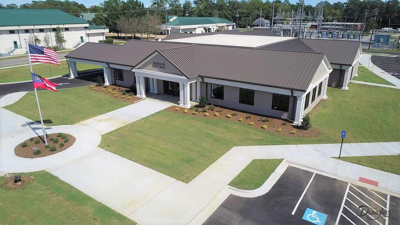 Aerial view of a modern single-story building labeled Douglas City Hall, with brown roof, columns, flags, landscaped grounds, parking lots.