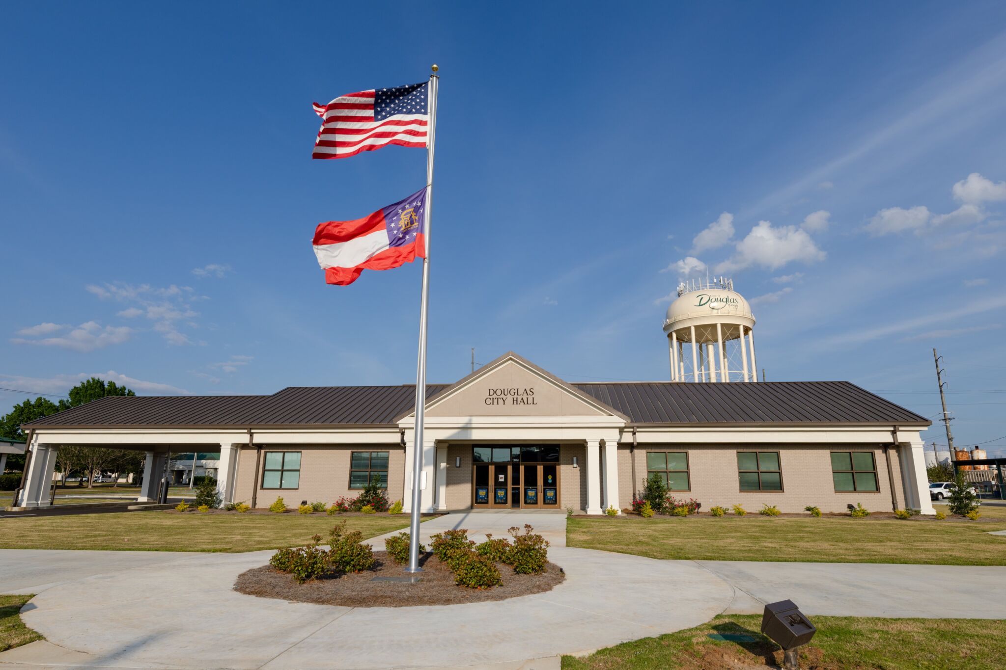 A modern building labeled Douglas City Hall with US and Georgia flags in front, and a water tower labeled Douglas under a blue sky.