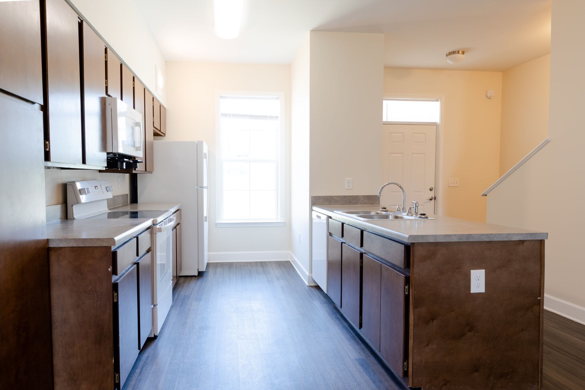 Modern kitchen with dark wood cabinets, white stove, microwave, refrigerator, double sink, window with natural light, light walls.