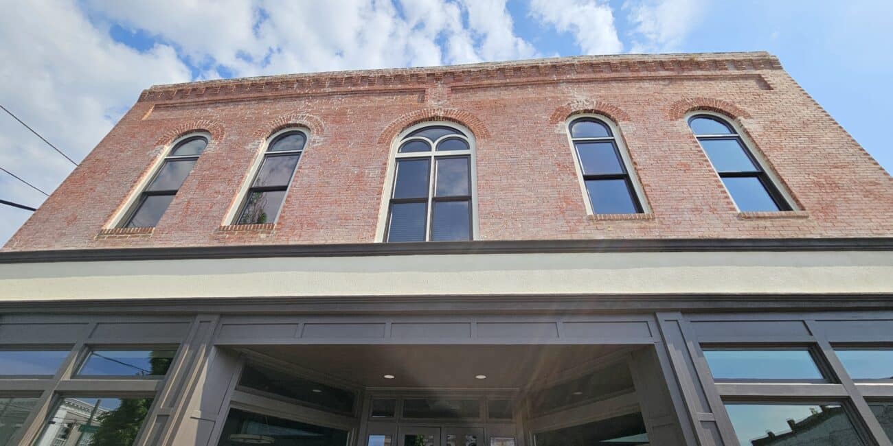 Low-angle shot of a historic brick building with arched second-floor windows and modern glass entrance below, under a partly cloudy sky.
