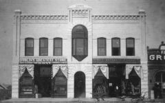 Historic black-and-white photo of a two-story brick building with arched doorway, large window, and signs for Dublins Greatest Store and Gilbert Hardware Company on the ground floor.