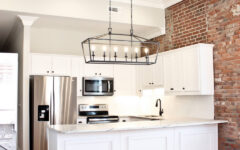 Modern kitchen featuring white cabinets, stainless appliances, brick accent wall, wood floors, and a bright minimalist design.
