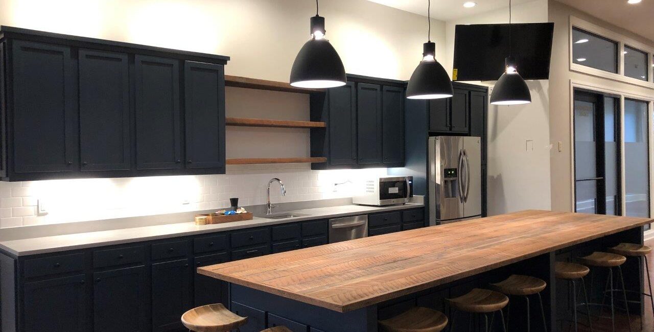 Modern kitchen with dark cabinets, open shelves, stainless steel appliances, a long wooden island, metal stools, and pendant lights.