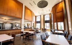 A spacious modern restaurant with high ceilings, arched windows, chandeliers, wood panels, marble tables, and a bar in back.