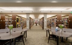 Spacious, bright library with bookshelves, round tables, chairs, flower vases, and tissues. Quiet, organized space for study or reading.