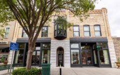 Two-story brick building with large arched and rectangular windows, a glass-door entrance, tree out front, and handicapped parking sign.