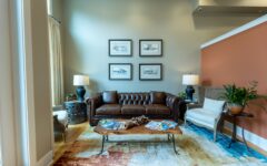 Cozy living room with brown leather sofa, side tables with lamps, an armchair, coffee table with magazines, plant, and patterned rug.