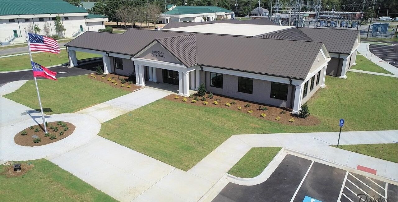 Aerial view of a modern, single-story building labeled Douglas City Hall with landscaped lawn, two flagpoles, parking, and roads.