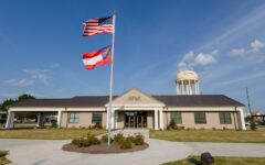 A one-story building labeled Douglas City Hall with American and Georgia state flags and a water tower labeled Douglas under a blue sky.