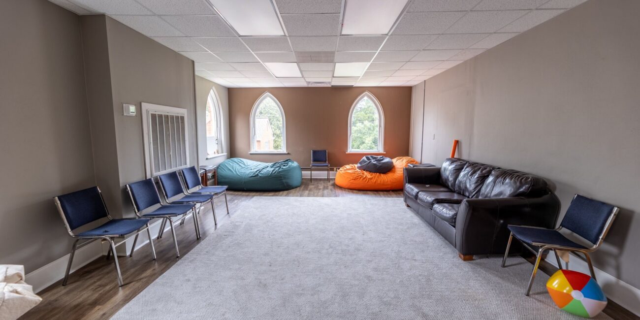 Cozy room with arched windows, bean bags, blue chairs, brown leather sofa, a beach ball, gray carpet, and natural light.