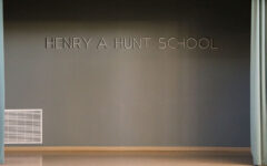 A stage with teal curtains drawn aside, revealing a gray wall with the words HENRY A. HUNT SCHOOL in large letters above a floor vent.