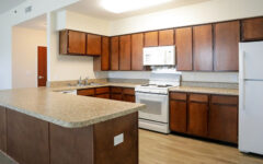 Spacious kitchen with brown wooden cabinets, white appliances, and a large L-shaped granite island on a wood floor.
