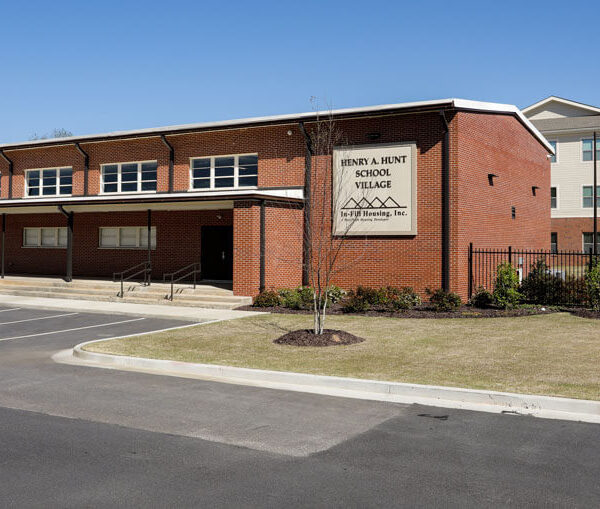 A modern two-story brick school building with a sign reading Henry J. Avery School Village, surrounded by parking lot, grass, and trees under a clear blue sky.