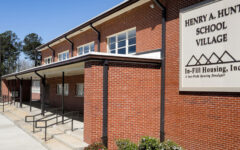 A red-brick building with a sign reading Henry A. Hunt School Village, In-Fill Housing, Inc. Ramps and sidewalks lead to entrances.