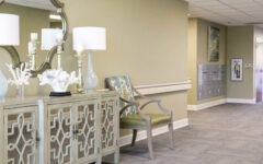 Hallway with pale green walls, a console table with decor, two green chairs, mailboxes along the wall, and natural light.