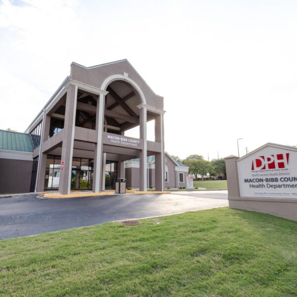 Exterior of Macon-Bibb County Health Department with a large covered entrance and Department of Public Health sign on grassy lawn.