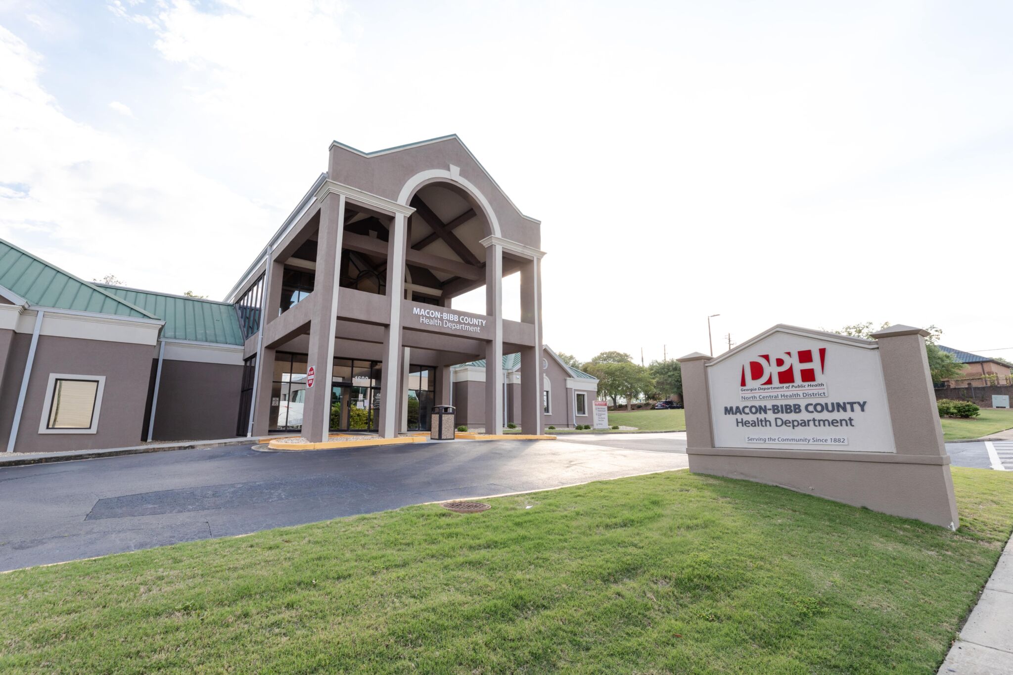 Exterior of Macon-Bibb County Health Department with a large covered entrance and Department of Public Health sign on grassy lawn.