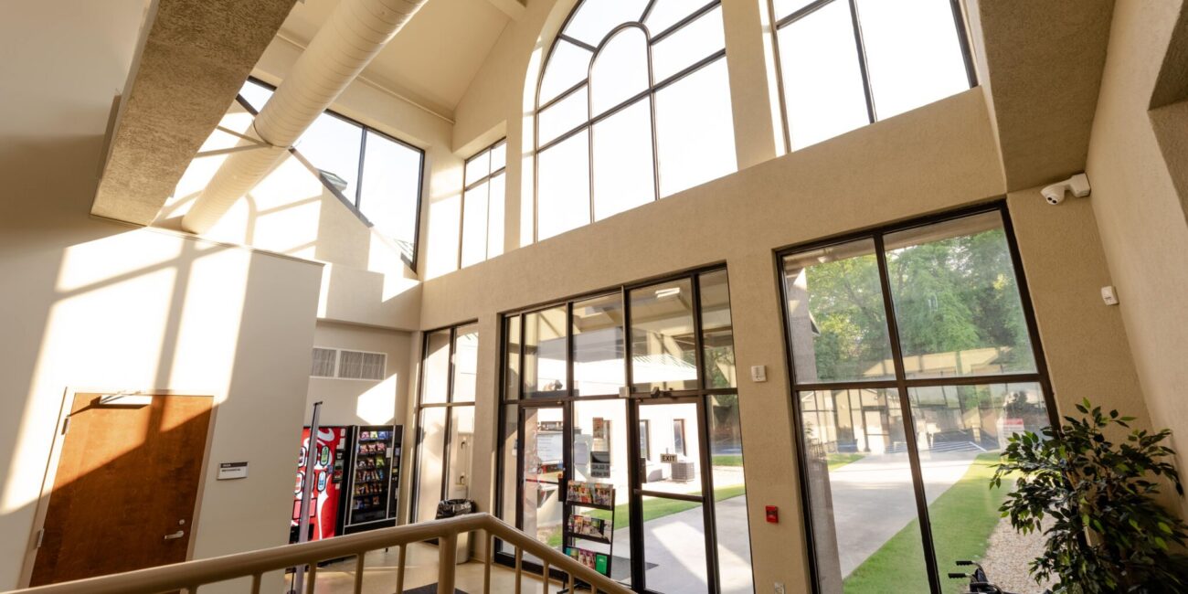 Bright, spacious lobby with tall windows, lots of natural light, staircase, vending machines by entrance, plant, and courtyard view.