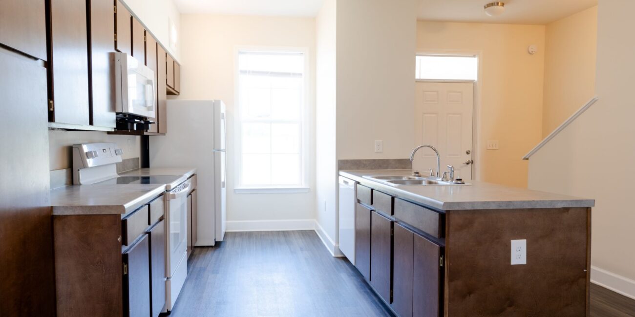 Modern kitchen features dark wood cabinets, stainless appliances, white fridge, island sink, and bright natural light from window.