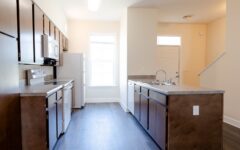 Modern kitchen features dark wood cabinets, stainless appliances, white fridge, island sink, and bright natural light from window.