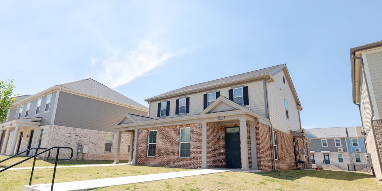 A two-story brick and siding house with black shutters and a black front door sits on a grassy lawn under a blue sky.