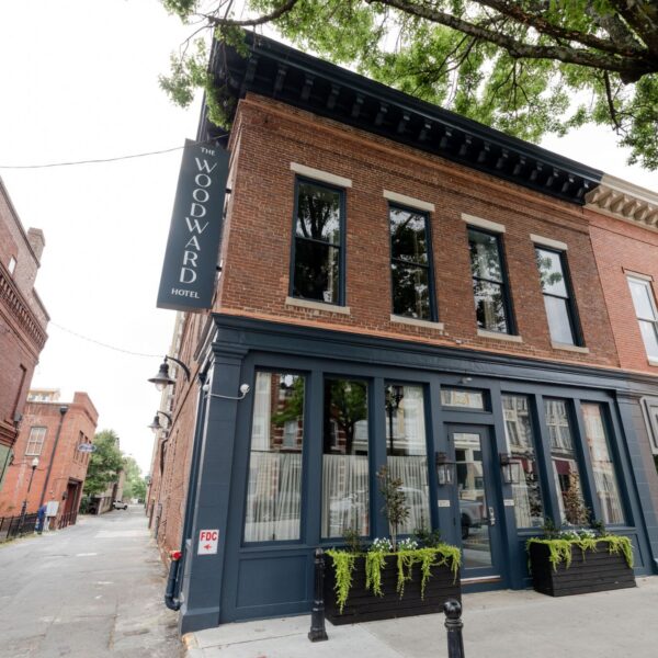 A two-story brick building with a sign reading Woodward Hotel hangs above the entrance. Large windows, planters, and Moon Club nearby.