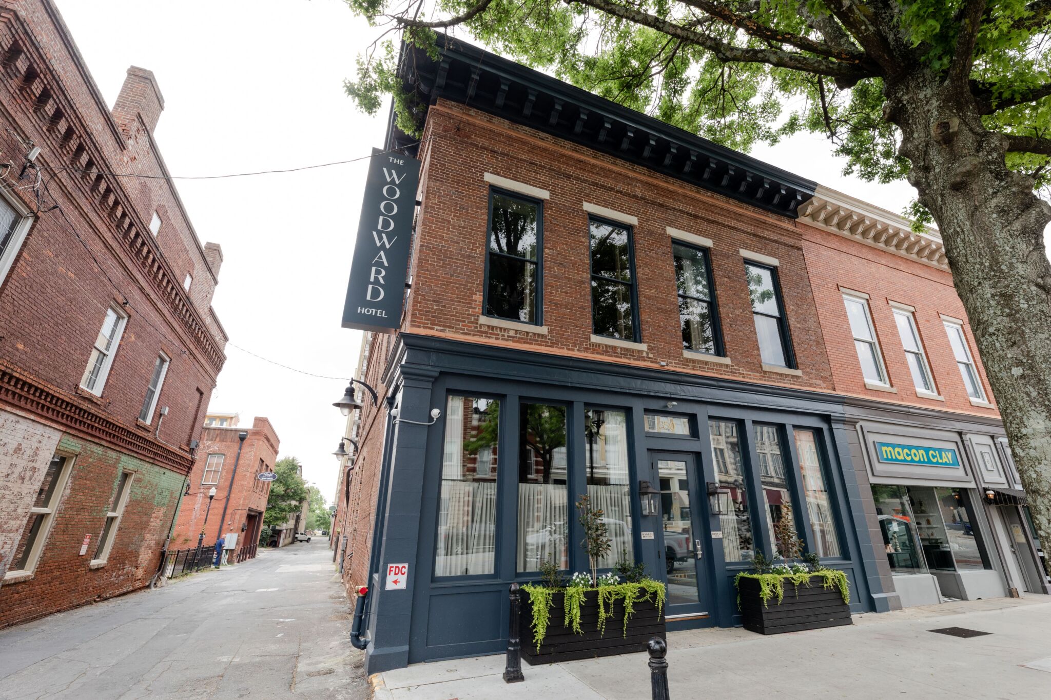 A two-story brick building with a sign reading Woodward Hotel hangs above the entrance. Large windows, planters, and Moon Club nearby.