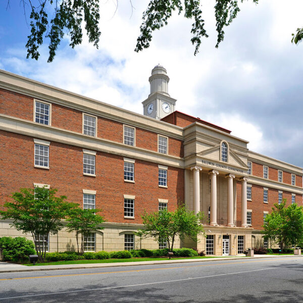 Large brick and stone building with tall columns, clock tower, many windows, and trees beneath a partly cloudy sky.