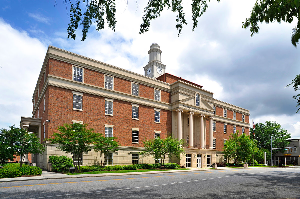 Large brick and stone building with tall columns, clock tower, many windows, and trees beneath a partly cloudy sky.