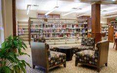 Cozy library seating with four patterned chairs around a round table on carpet. Book-filled shelves line the bright, well-lit space.