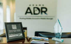A framed 2019 Preservation Award, a crystal trophy, and brochures on a wooden desk with Adams ADR logo blurred in the background.