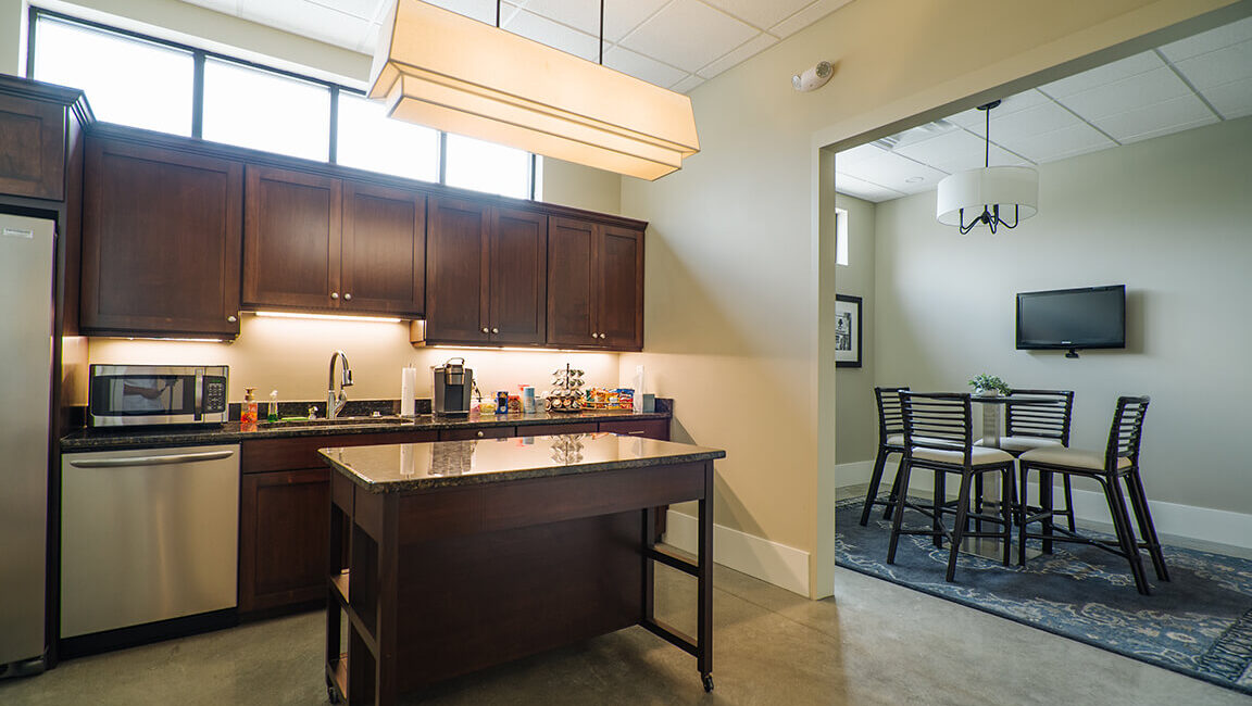 Modern kitchen with dark wood cabinets, stainless steel appliances, central island, and adjacent dining area. Bright, minimalist design.