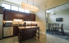 Modern kitchen with dark wood cabinets, stainless steel appliances, central island, and adjacent dining area. Bright, minimalist design.