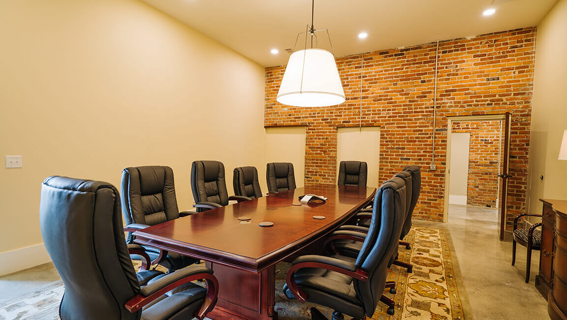 Conference room featuring a long wooden table, ten black leather chairs, exposed brick walls, overhead lights, and a rug under the table.