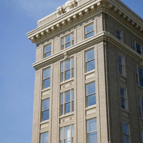 A beige brick building with decorative cornices and large windows stands under a blue sky, topped with ornate architectural moldings.