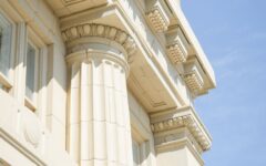 Close-up view of a beige stone building with fluted columns, ornate cornices, and classical details under a clear blue sky.