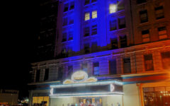 A group of people stand outside a theater entrance at night, marquee glowing; the building is lit with blue and orange lighting.