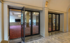 A grand hallway with marble floors and arched ceilings leads to a glass-walled conference room with red carpet and chandeliers.