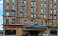 A historic brick hotel with a sign reading Grand Opera House above the entrance, two cars parked in front, large windows on the façade.