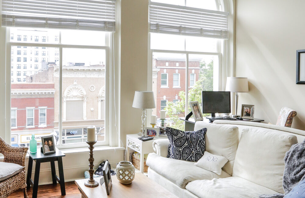 Bright living room with arched windows, white sofa, armchair, coffee table decor, lamps, photos. City view. Cozy modern vibe.